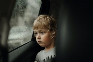 A cute little blond boy looking out of the car window on a rainy day. Bad weather mood, depression N